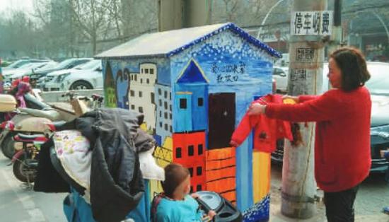 一位女士準備將一件舊童衣投進愛心回收箱