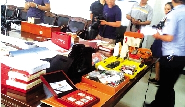 在警方展示赃物的现场,各种玉石、陶瓷、珠宝、金表、类似兵马俑的古董、冬虫夏草、古书、纪念币、邮票、笔记本电脑、平板电脑等满满一桌子物品着实让人看得眼花缭乱。