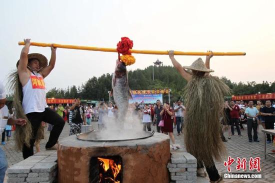 现场气氛喜庆热闹，众人围坐，灶台高筑，一根根比胳膊还粗的劈柴被塞进灶膛燃起熊熊烈火。三条1米多长的“鱼王”被几名壮汉抬上灶台，“西施”美女从古代穿越而来，不但拎起菜刀上阵片鱼，待美味鱼汤做成，还迈起莲步给大家送汤，引起众人欢呼雀跃。图为灶台高筑，鱼王被抬上准备下锅。王中举摄