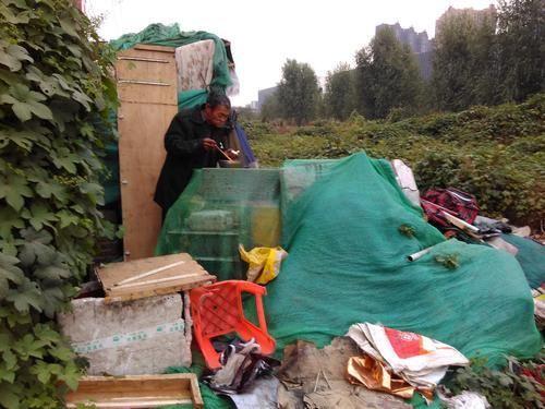 老人從附近飯店要回來的一些殘渣剩飯，在火上熱一熱后，蹲在棚邊吃了起來。