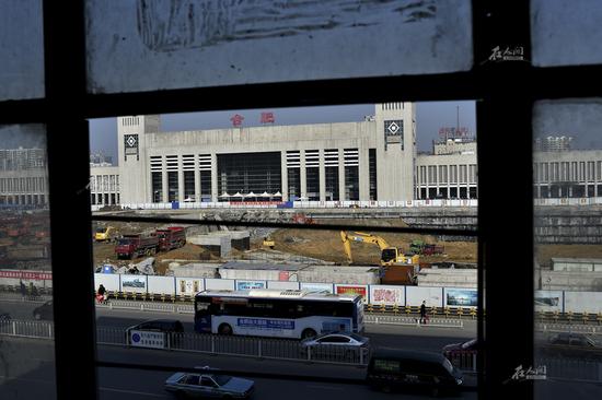 這座大型商城曾經(jīng)是當(dāng)年合肥新火車站建成時(shí)站前廣場(chǎng)的標(biāo)志性建筑，商鋪在1996年就賣出了8000多元一平米的“天價(jià)”。因?yàn)橐恢蔽赐ㄟ^(guò)經(jīng)消防驗(yàn)收、產(chǎn)權(quán)結(jié)構(gòu)復(fù)雜等問(wèn)題，盡管這座商城坐擁著合肥最優(yōu)越的地理位置，卻從未享受過(guò)繁華。圖為透過(guò)新鴻安商城損壞的窗玻璃，可以看到對(duì)面的合肥火車站，兩者之間就隔著一條站前路。