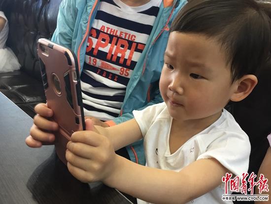 5月14日,天津一家餐厅,一名3岁儿童在等餐期间,用家长的手机聚精会神玩儿游戏。中国青年报·中青在线记者 张国/摄
