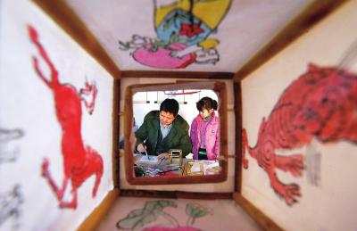 木版灯笼画传承人张四清在做灯笼画时,孙女在一旁观看。