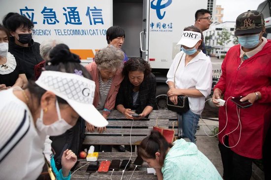 8月6日,人们在黑龙江省海林市长汀镇一广场上的应急通信车前与外界通话