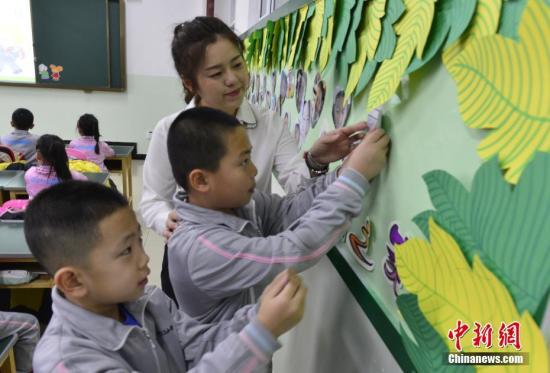 资料图：学生在老师的指导下将自己的照片贴上笑脸墙。中新社记者 刘新 摄
