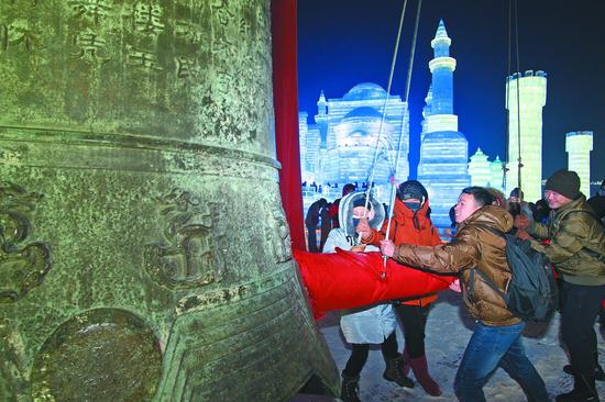 图为游客在哈尔滨冰雪大世界敲响新年钟声。