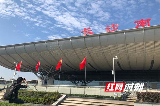 一位旅客正在国旗下以“长沙南”三个字为背景,拍照留念。