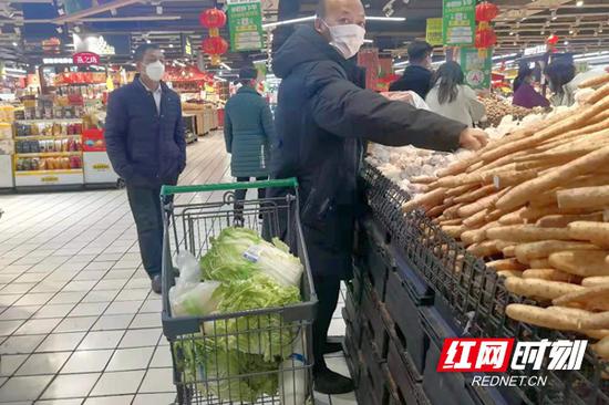一位顾客的购物车里装着大白菜、白萝卜等蔬菜。