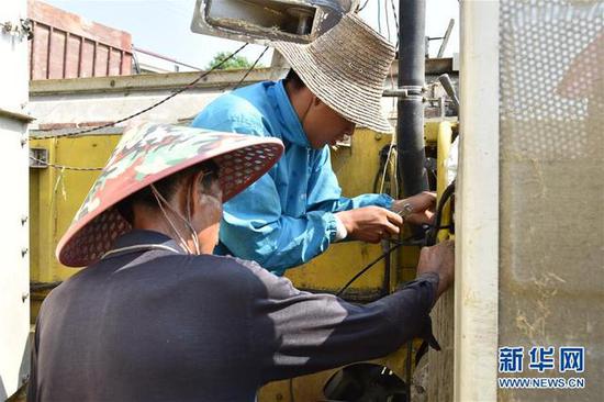 7月15日，在湖南衡东县洣水镇采霞村，村民康文俊（右）和父亲一起维修收割机。 新华社记者 白田田 摄