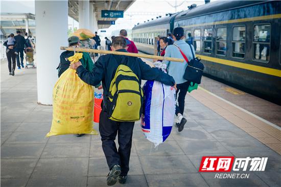 站台上一名乘客挑着行李货物，即将踏上回家的绿皮火车。