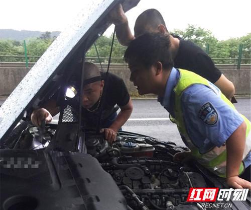 交警李贡与维修人员冒雨检修高速路抛锚汽车。