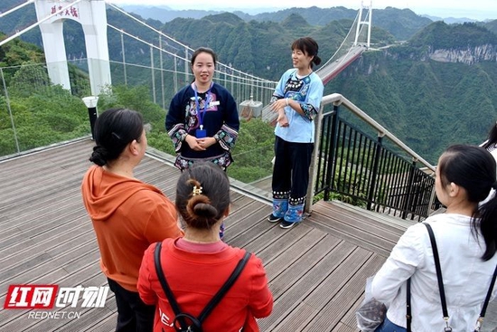  龙连智（穿深蓝苗服）在为游客介绍矮寨大桥和天桥仙居。