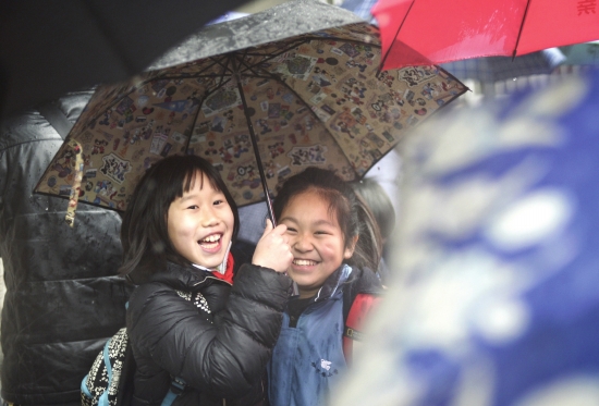 2月18日，长沙中小学开学第一天，砂子塘小学的两名女生开心地共用一把伞走出校园。图/记者辜鹏博