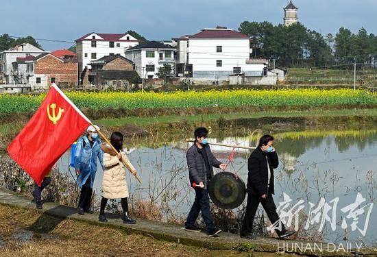 (2月9日,洞口县高沙镇云峰村,党员志愿者在走村穿巷敲锣提醒村民加强疫情防控。滕治中 摄)