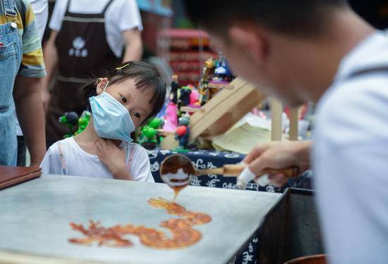 ▲ 6 月 2 日晚,长沙,一位小女孩饶有兴趣地观看廖师傅制作糖画
