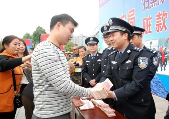 图为民警将赃款返还给受害群众。
