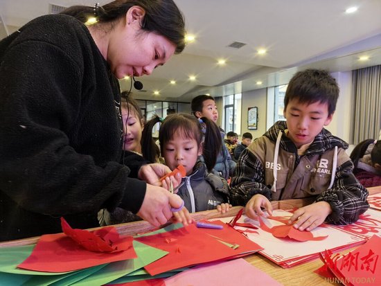 雨湖区和平社区活动室，孩子们跟着老师剪纸。