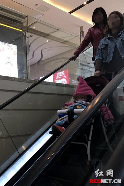 一家长单手推婴儿车乘扶梯,婴儿车的前排车轮悬空。