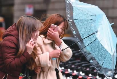 长沙市五一大道，市民打着雨伞在风雨中前行。