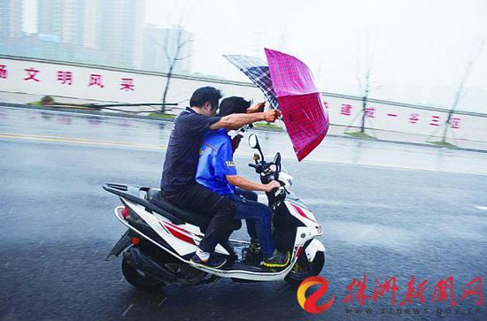 昨天，白石港路，暴雨中，一名男子搭乘摩托车，举着两把伞顶雨前行，看着十分危险（记者 谢慧 摄）