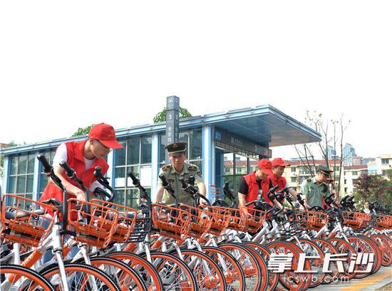 岳麓区城管工作人员和来自长沙市职业技术学院的志愿者们正在将乱停乱放的共享单车移到规定区域并摆放整齐。资料图片