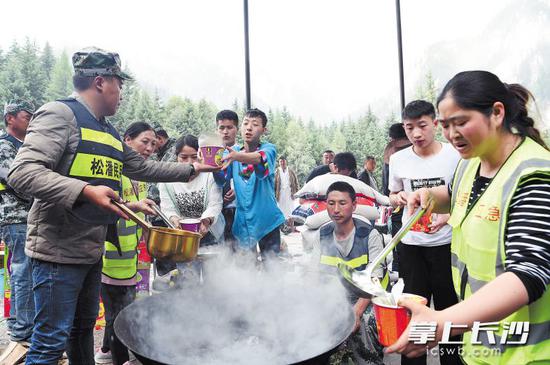 8月9日，在四川省九寨沟县九寨天堂洲际大饭店停车场，救援人员为滞留游客提供食品。
