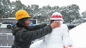 12月27日，长沙市开福区湘江中路，一名穿着制服的工作人员堆起一个戴安全帽的小雪人。