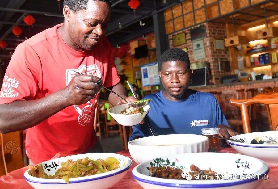 6月10日，河村非洲文化园，Tom（汤姆）（左）吃早餐时用菜汤泡饭吃。非洲艺人们都喜欢汤泡饭，很喜欢吃湖南菜，也熟练地学会了使用筷子。