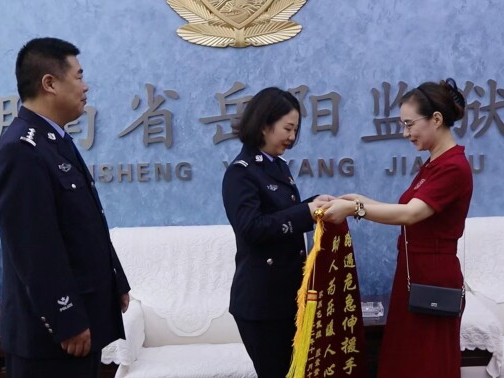 图为在省岳阳监狱副监狱长李绍元（左）的见证下，小包母亲（右）亲手将锦旗交至谢扬文（中）手中。
