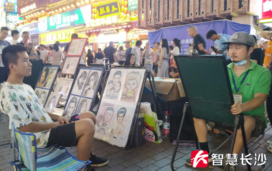 图为黄兴路步行街上的街头艺人(右)在为游客画肖像(剑裘 摄)