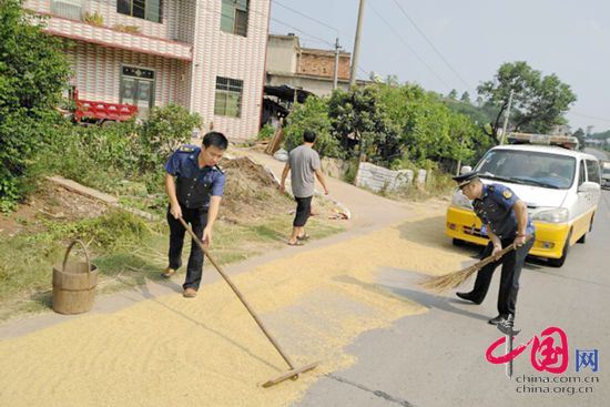 路政人员帮助农户将稻谷收起，确保交通安全