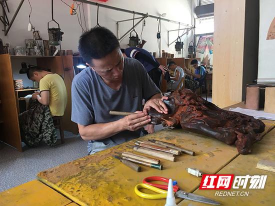 湖南省工艺美术大师肖韶山拿着雕刀一笔一画细致地雕刻名为《对弈》的酸枝红木雕。