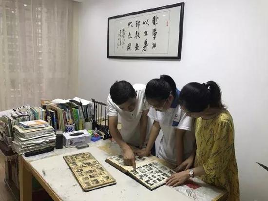 方汞和妻子何思佳与女儿一起翻阅老照片。墙上悬挂家训“非学无以立身,非教无以立国”。(袁汝婷 摄)