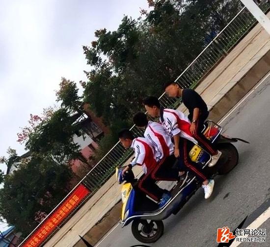 一名十来岁的少年骑着一辆电动车搭载着3名同伴骑行在马路上。