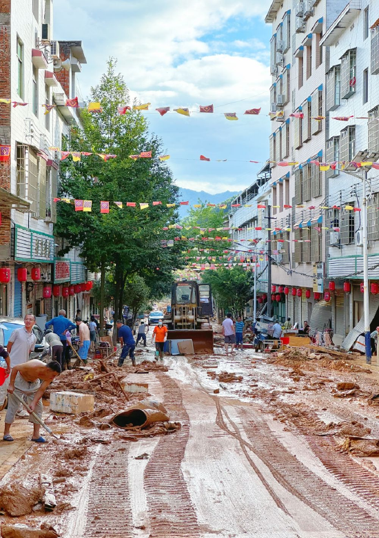 7月30日,在资兴市八面山瑶族乡集镇,当地干部群众正在清理街道上的淤泥。