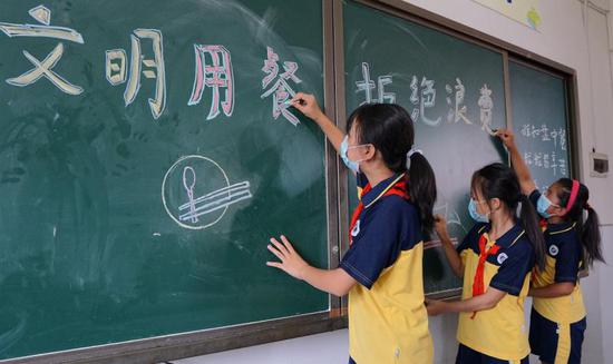 同学们在黑板上写上新学期班会主题“文明用餐,拒绝浪费”