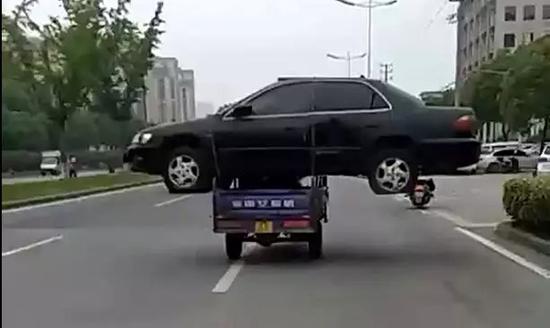 嫌拖车费贵 男子用三轮车“扛”着报废轿车路上飞奔