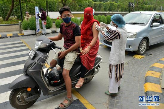 5月17日,在印度诺伊达的一个“免下车”新冠疫苗接种点,医务人员为一名女子接种疫苗。新华社发(帕塔·萨卡尔摄)