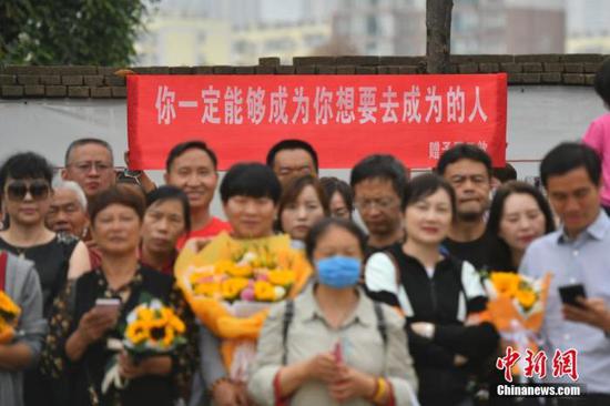 资料图:6月8日,云南省昆明市的考生结束2021年全国高考。图为考试结束后,一幅助考标语前有考生和家长合影留念。 中新社记者 刘冉阳 摄