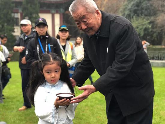 可爱的“紫金草女孩”从幸存者葛道荣老人手上接过象征和平与顽强的紫金草花种,并分发给徒步嘉宾。