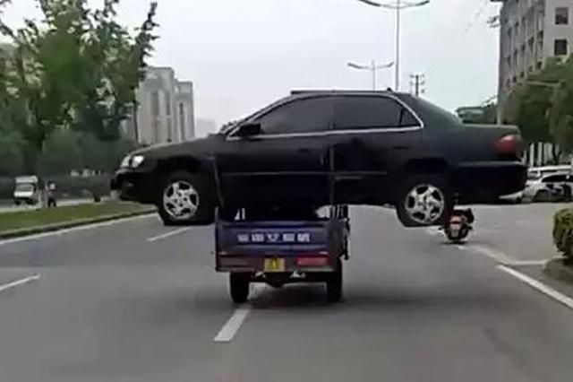 嫌拖车费贵 男子用三轮车“扛”着报废轿车路上飞奔