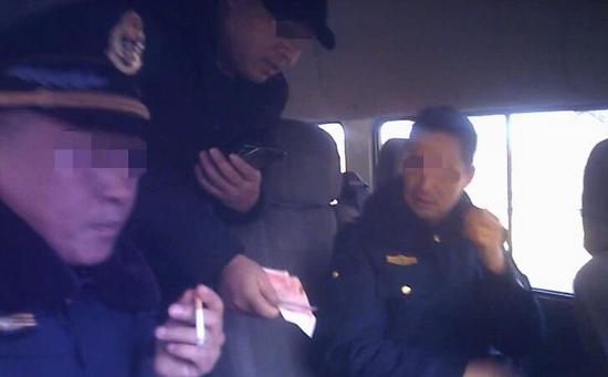 两名身着制服的交通执法人员，向超载货车司机收钱。视频截图