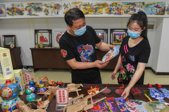 6月25日，在梨树县孤家子镇，农民画传承人钱洪满（左）和女儿钱璐研究农民画文创产品。