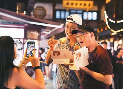 游客在上海豫园夜市开心地品尝当地特色小吃生煎包。 新华社记者 刘 颖摄