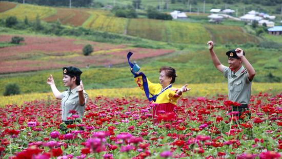 8月15日，在图们市日光山花海景区，边防官兵与朝鲜族老人漫步在花海美景中。