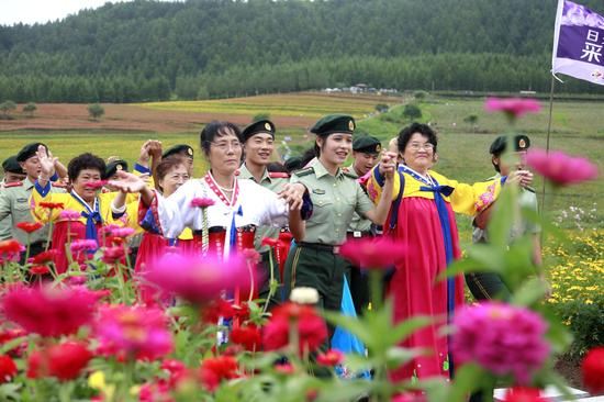 8月15日，在图们市日光山花海景区，边防官兵与朝鲜族老人漫步在花海美景中。