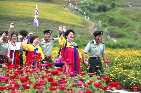 8月15日，在图们市日光山花海景区，边防官兵与朝鲜族老人漫步在花海美景中。