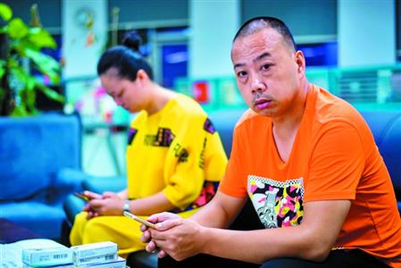 陈兴国接受记者采访,佟蓓则在一旁玩游戏。