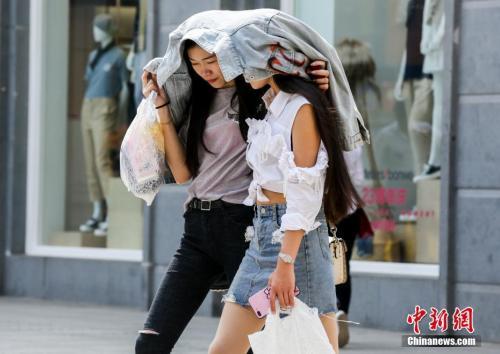 4月3日,武汉江汉路步行街上,两名年轻女性用外套遮挡火辣的阳光。当日,武汉主城区最高气温已达30摄氏度。 中新社记者 张畅 摄