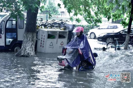 一位市民骑着电动车小心地在水中的道路上前行